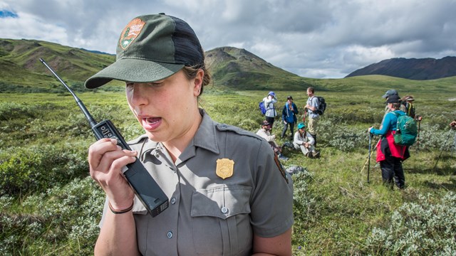 female ranger speaks into a radio near a group of hikers
