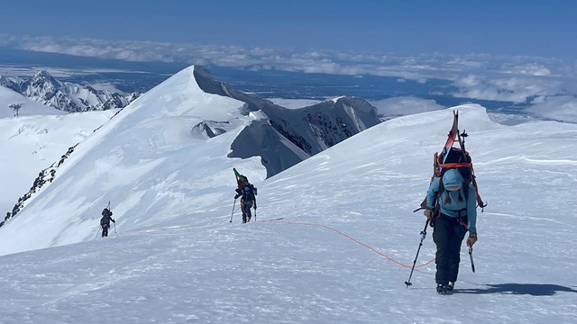 Mountaineers crossing a snow field carrying gear