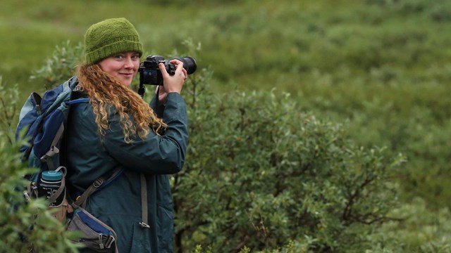 A woman holding a camera in raingear 