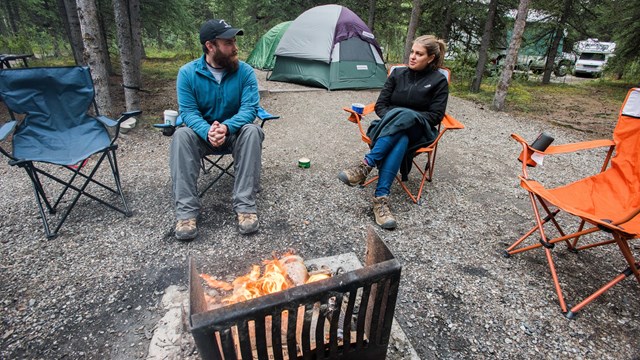 two people sitting in camp chairs near a fire