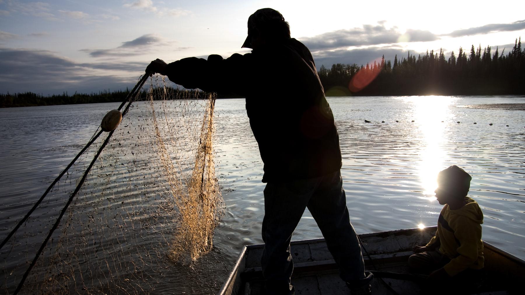 a man throws out a fishing net from his boat