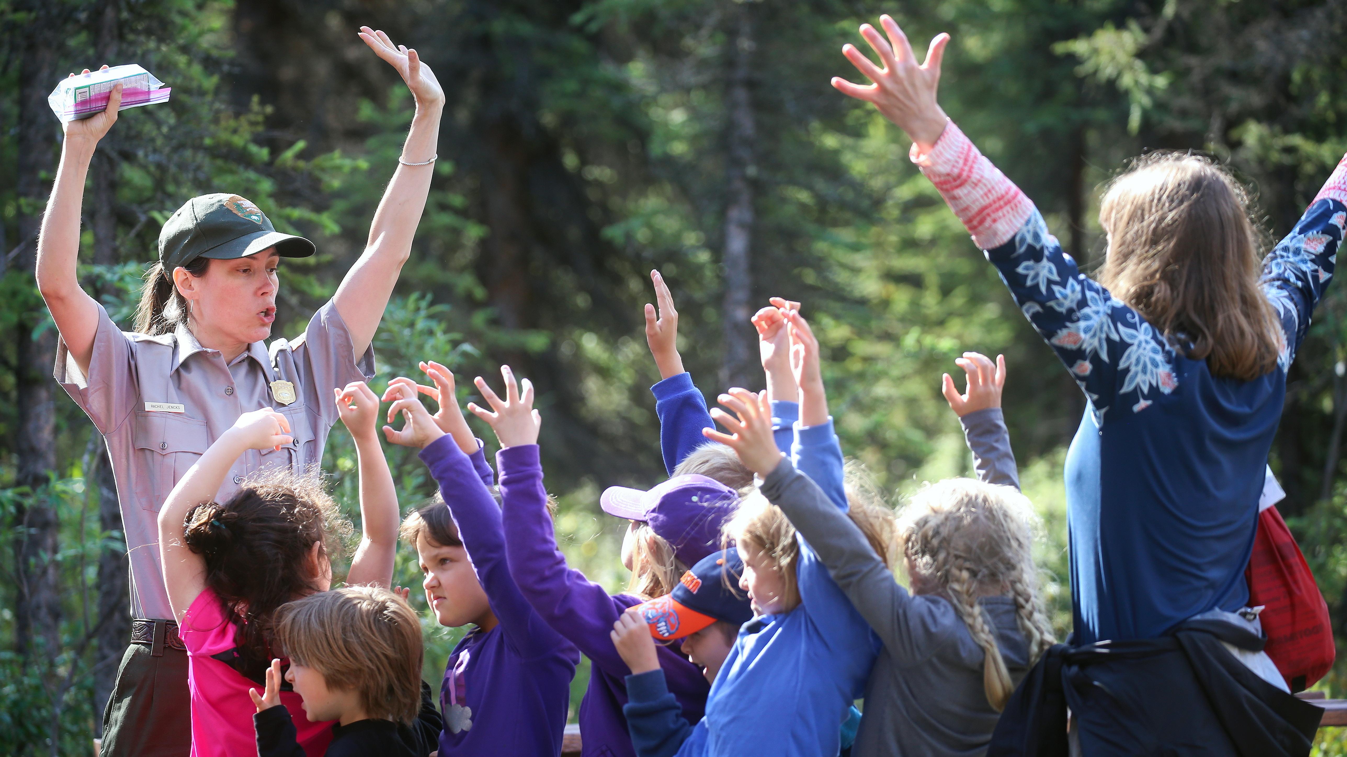 A ranger and kids stand with their arms in the air, making animal claws with their hands.