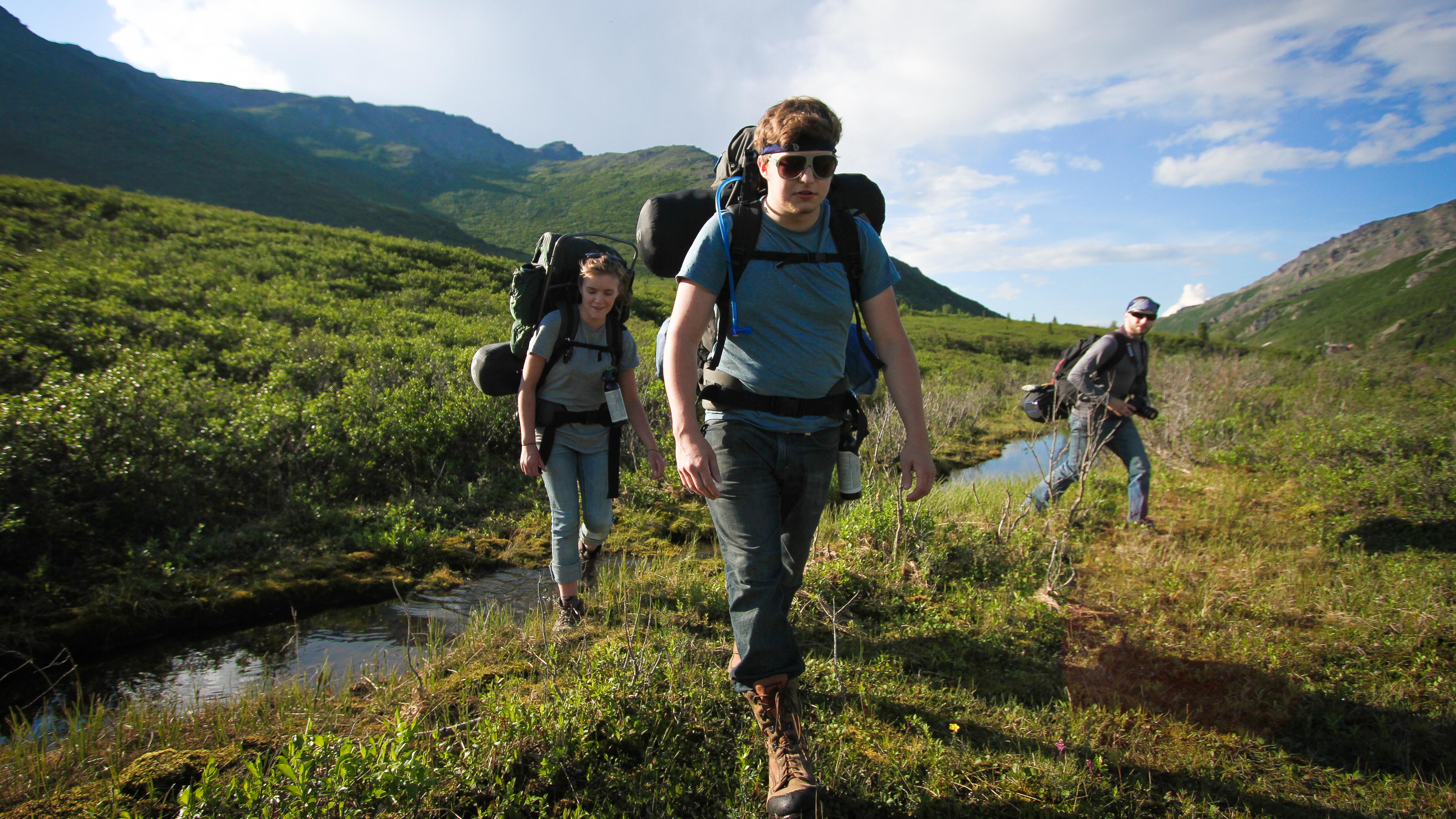 three people hiking through a small creek on a hill