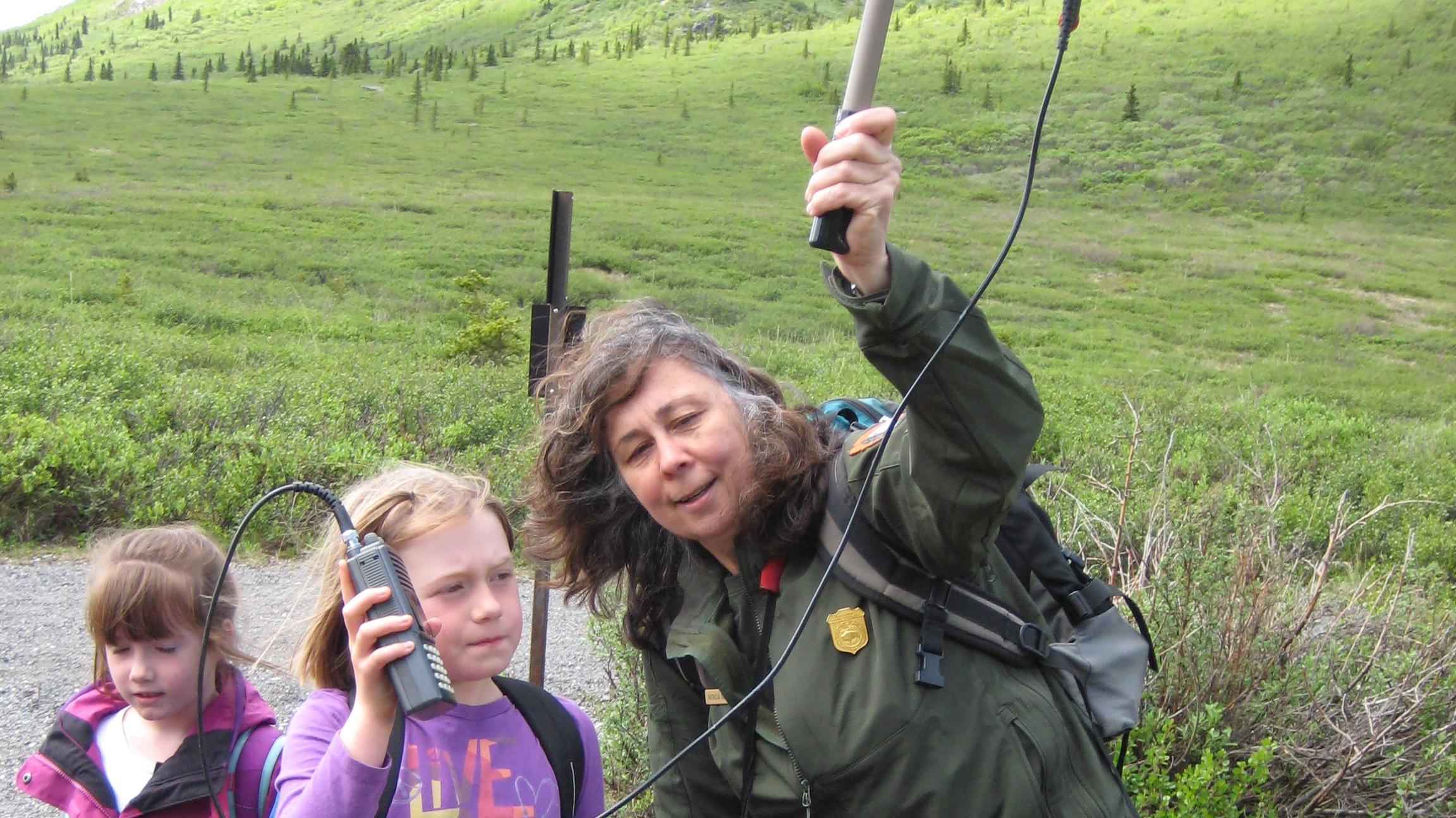a ranger holds up a radio tracking tool while talking to children