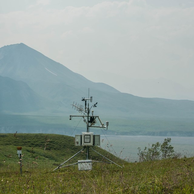 Weather monitoring equipment on a tundra hillside, with hazy mountains in the distance.