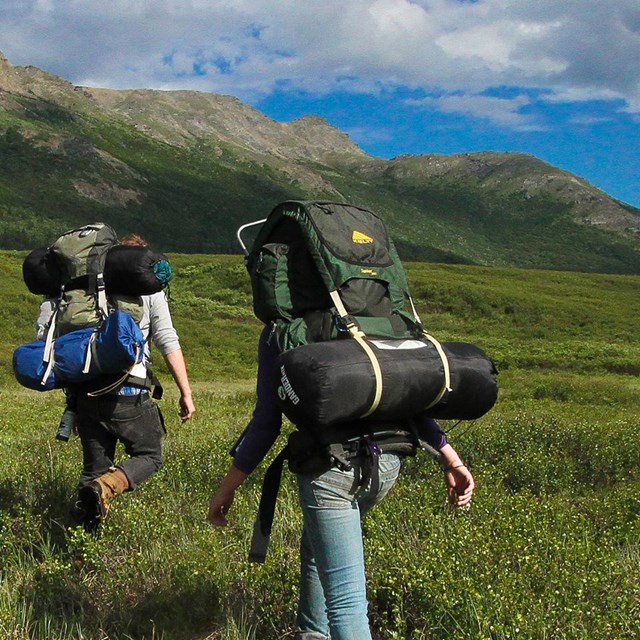 two backpackers trek across a grassy valley