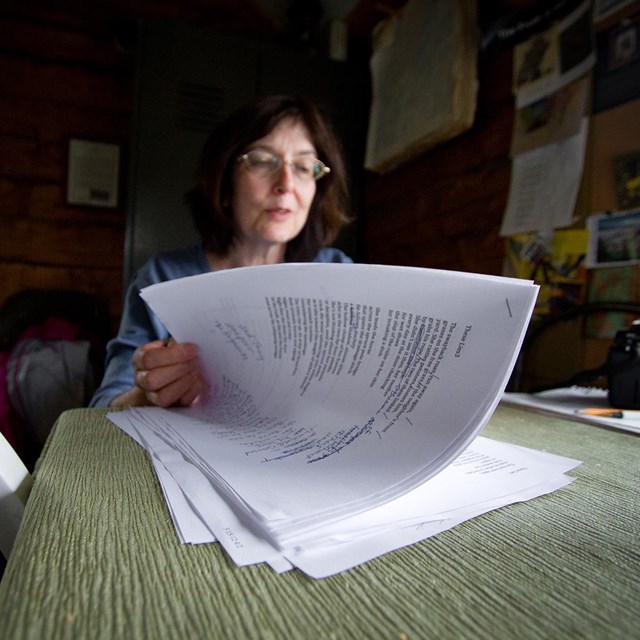 a woman sitting at a table reads through a stack of papers
