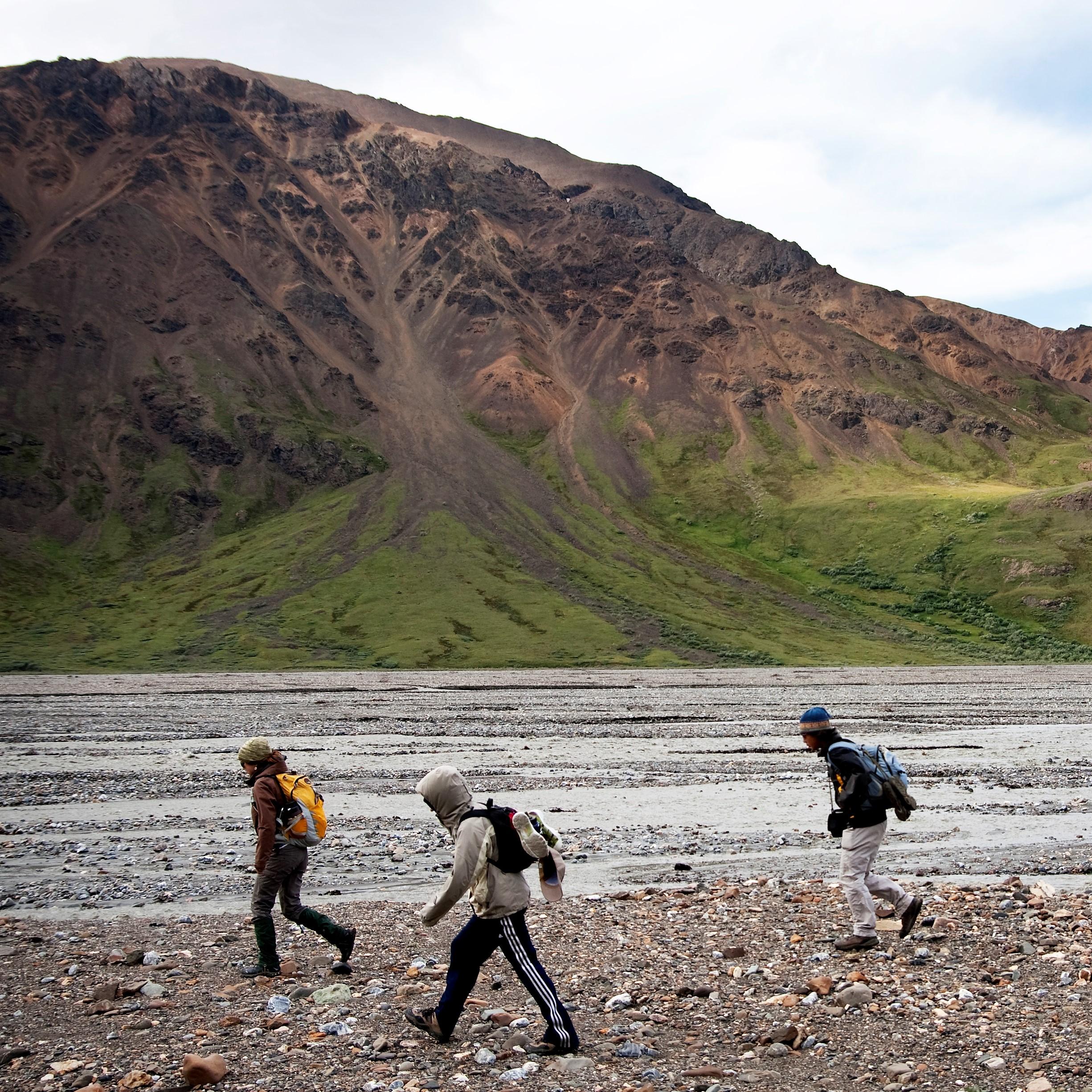 a group of young visitors hike along a gravel riverbank