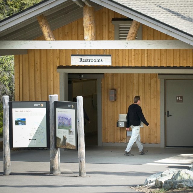 A man walks toward the door of a small wood building with a sign for restrooms.