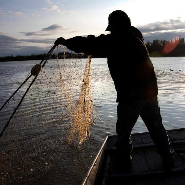 a man throws out a fishing net from his boat