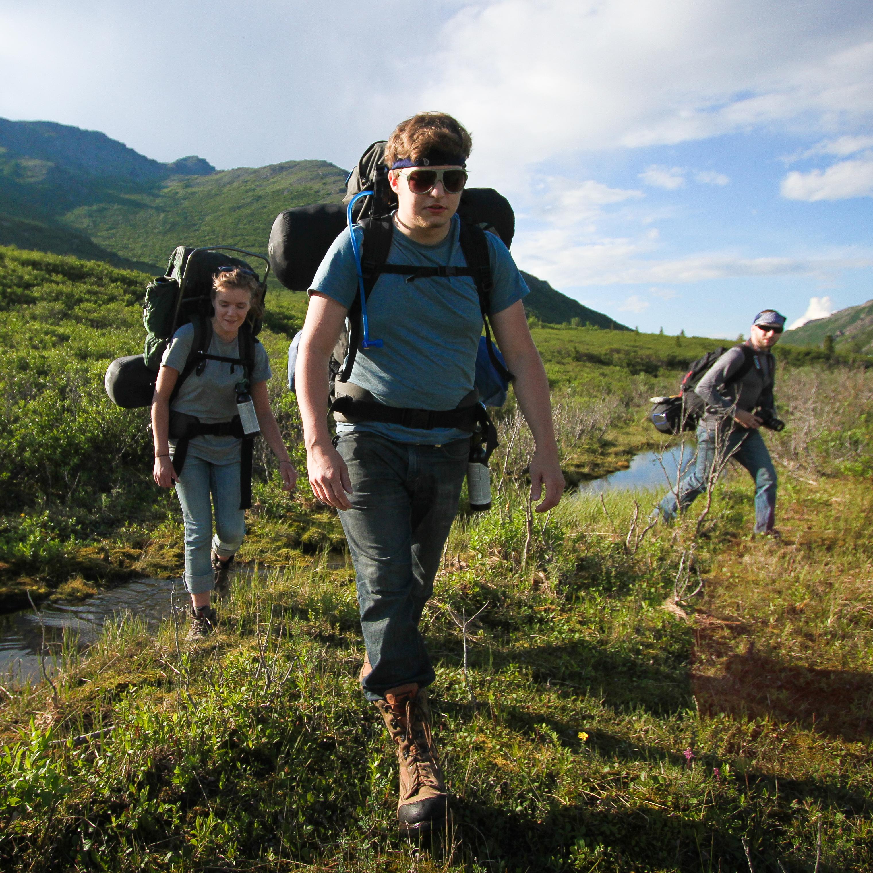 three people hiking through a small creek on a hill