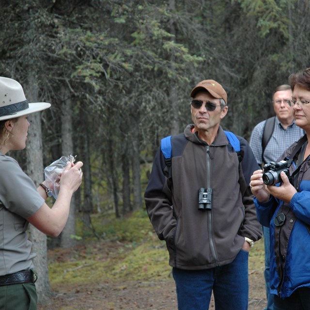 a female ranger shows a group of people an object on a trail