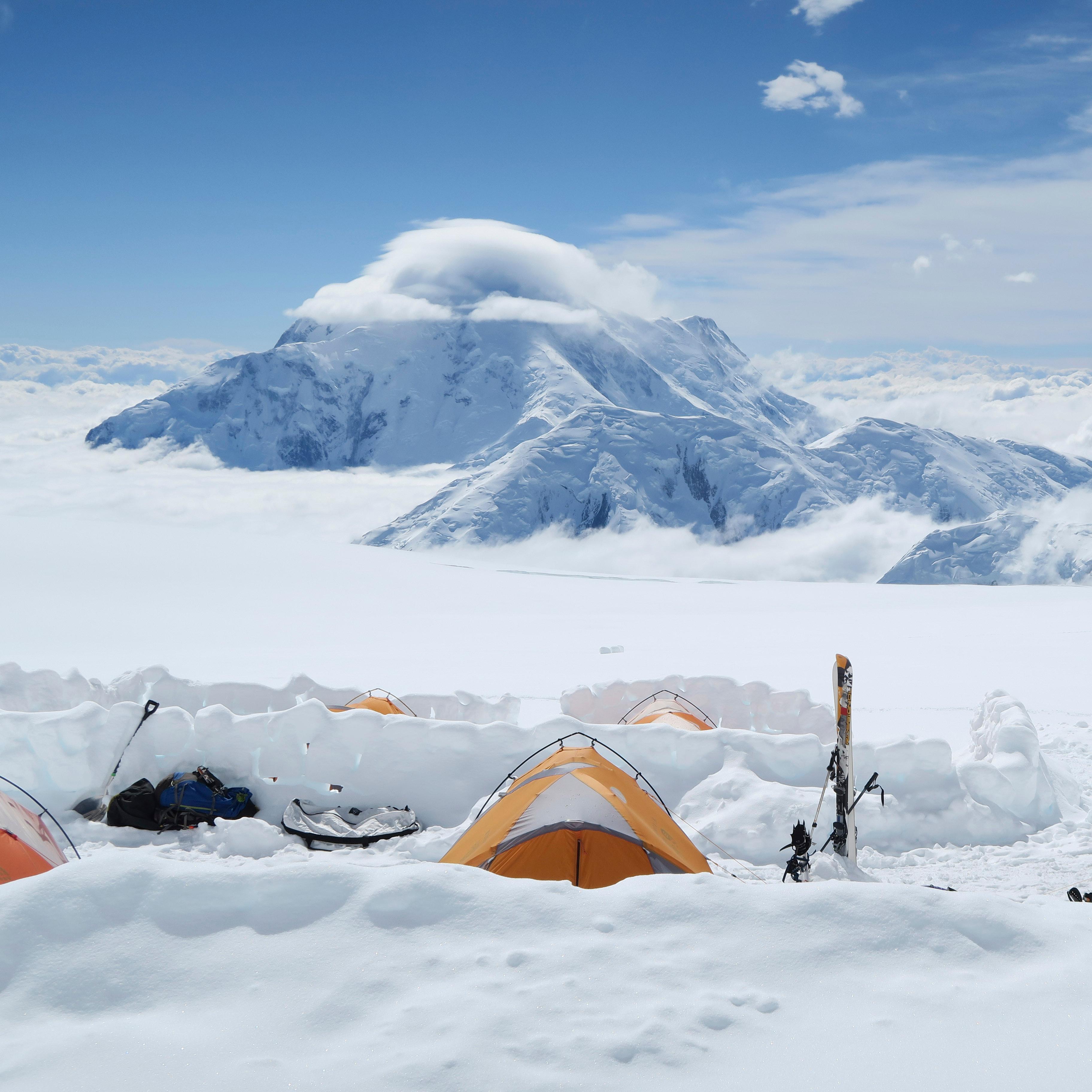 snowy, mountainous landscape with numerous people and tents in the distance