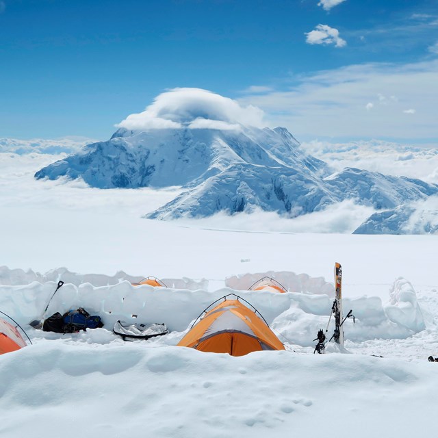 snowy, mountainous landscape with numerous people and tents in the distance