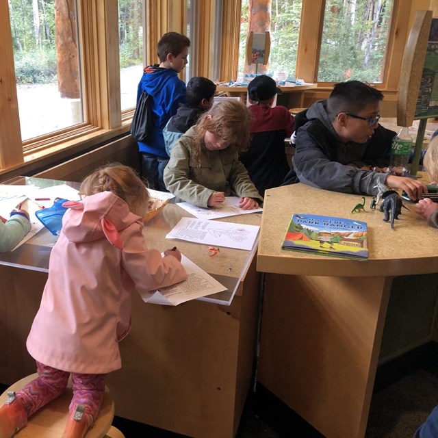 Kids work on coloring pages together around a table.