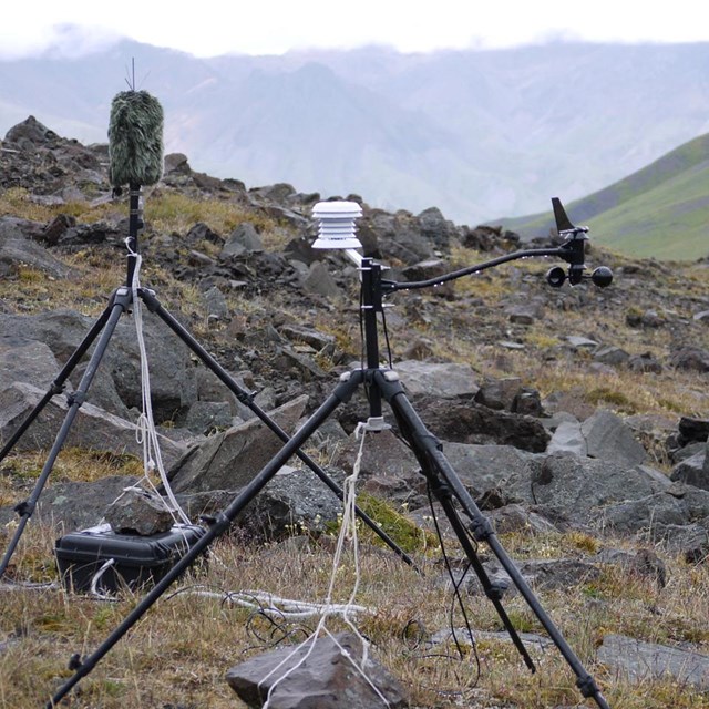 two tripods holding sound equipment sit on a rocky hillside