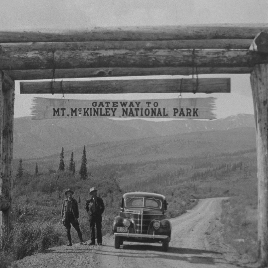 two people stand next to a car under a sign for Mt. McKinley National Park