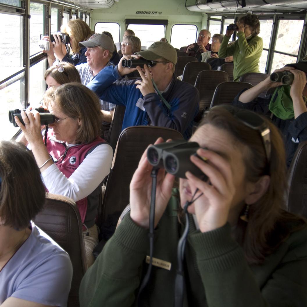 visitors on a bus use binoculars to look out the window