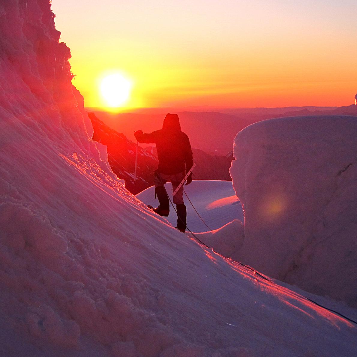 mountaineer on a snowy mountain backlit by a setting sun