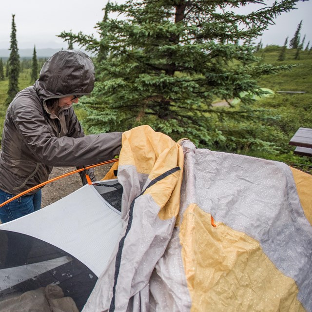 woman putting a rain fly on a tent