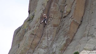 A woman reaches for chalk as she climbs Devils Tower