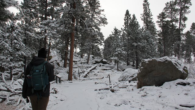 A hiker walks on a snowy trail.