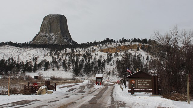 The welcome sign and entrance station in front of the Devils Tower monolith in the snow.