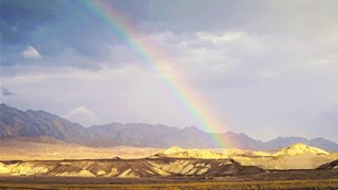 A rainbow reaches down to shimmering desert mountains.