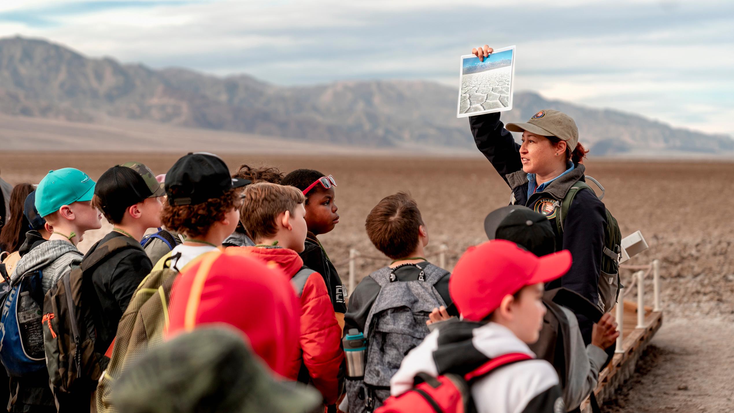 A uniformed employee showing students a demonstration with a mountain background.