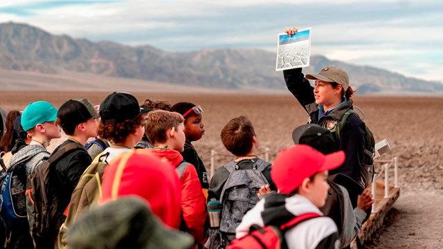 A uniformed employee showing students a demonstration with a mountain background.