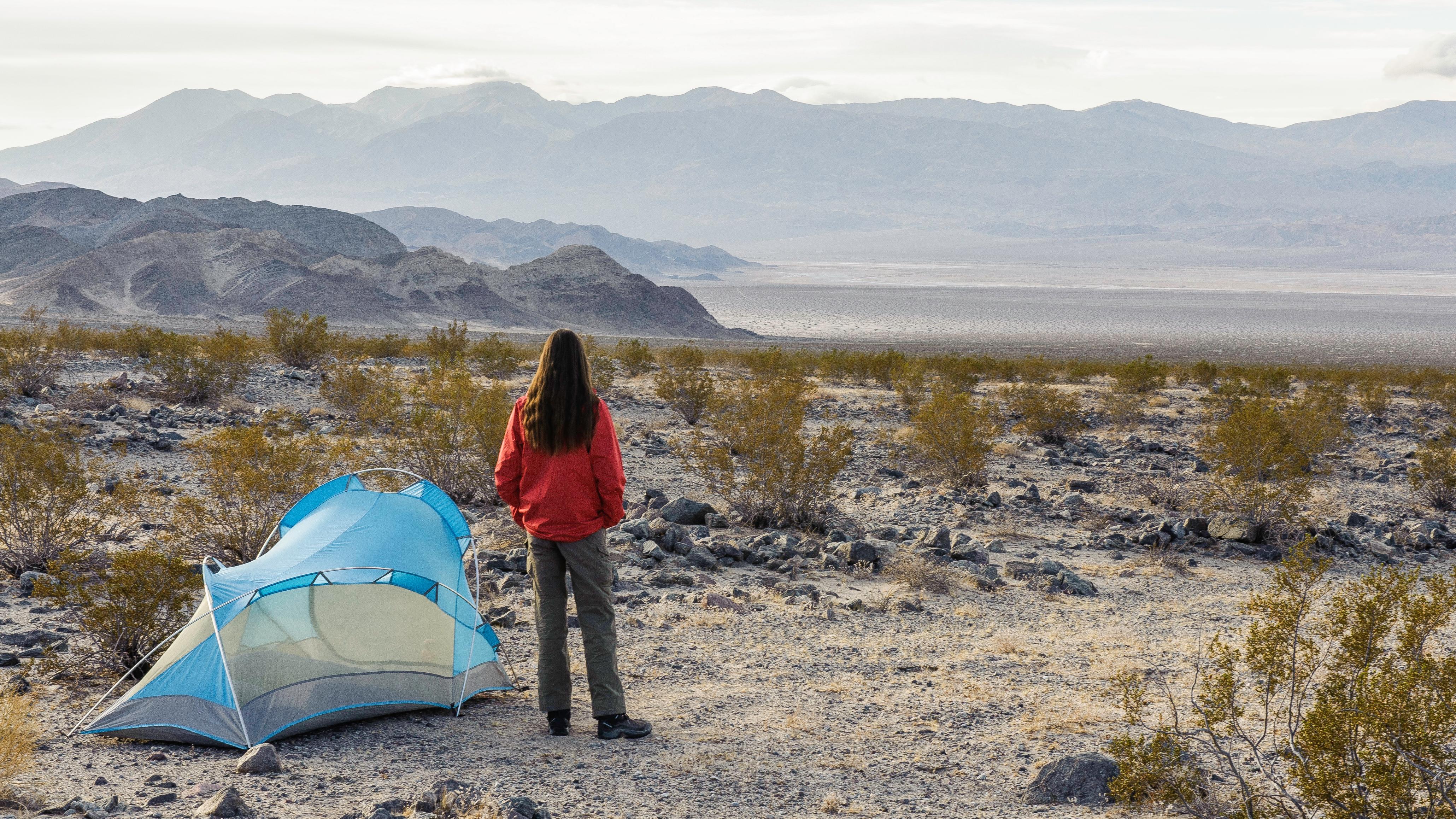 a camper stands next to a tent in desert scenery