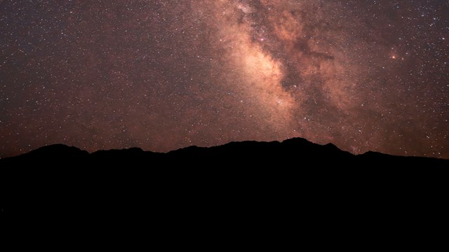 A night sky fills the frame, thick with stars. A wide, hazy band of light runs diagonally.