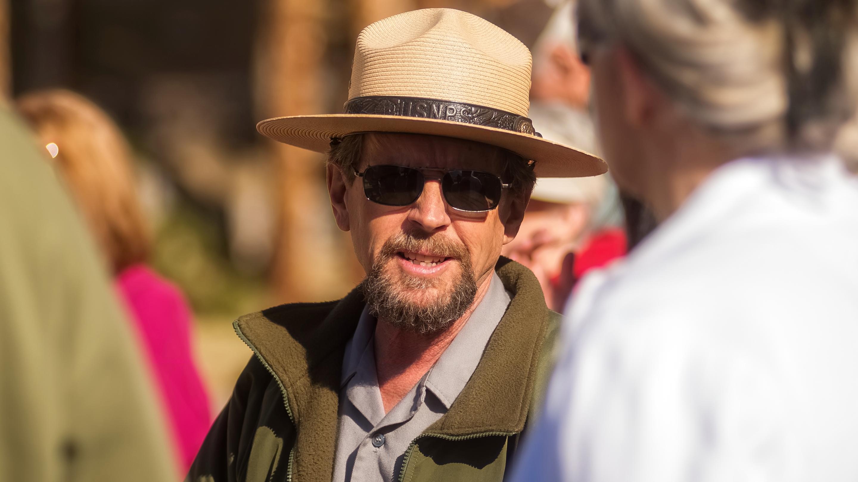 a ranger in a hat speaks with visitors