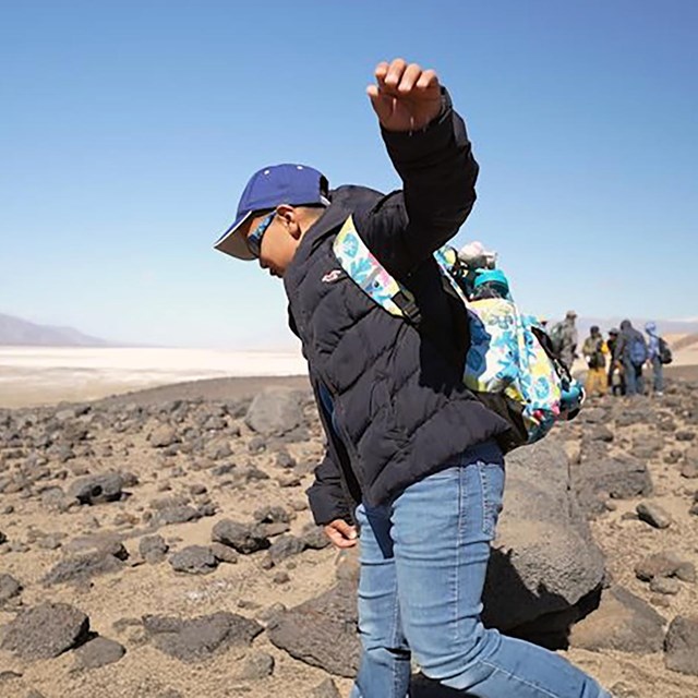 A young child in the foreground, hiking across a rugged, rocky desert terrain.