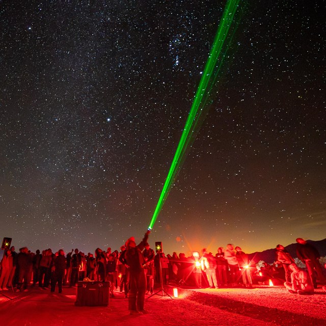 The photograph captures a night sky filled with stars above a group of people engaged.