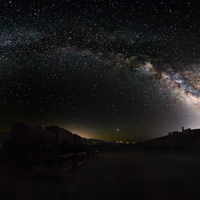 Bright stars dot the sky above a borax wagon made of two wooden carts and a metal water tank.