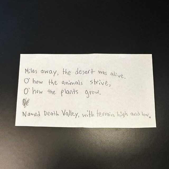 A piece of white paper sitting on a black background. Written in pencil on the paper is an acrostic.