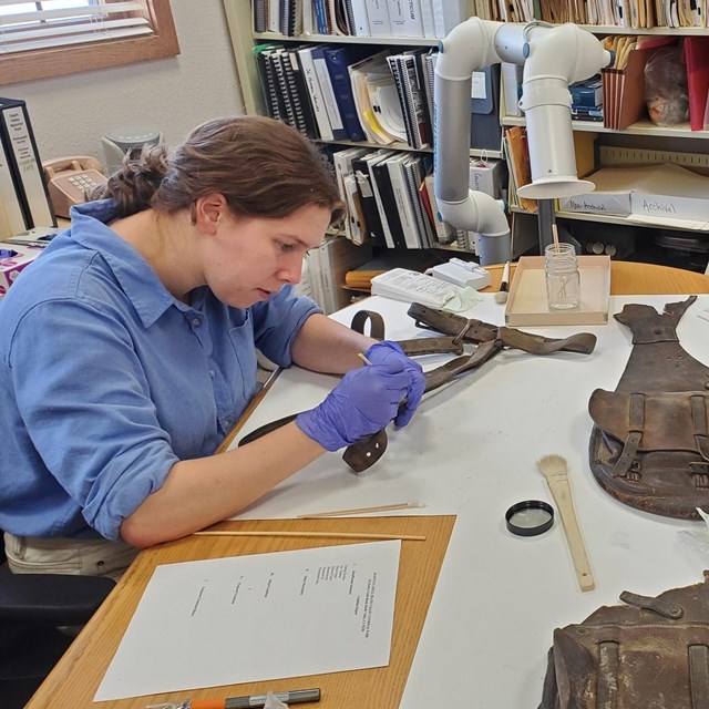 Two individuals wearing gloves and holding conservation equipment, bent over a table cleaning.