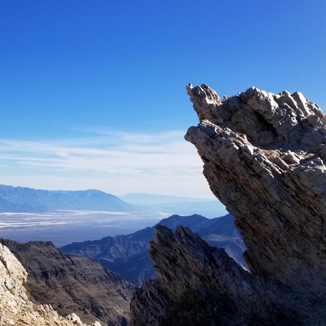Sharply angled rock outcrops over high views of a broad, low valley of salt flats bordered.