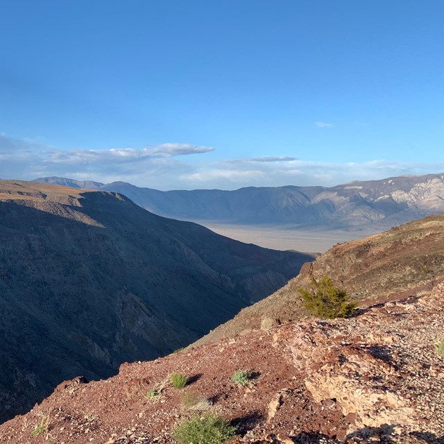 A view over a shadowed canyon with a flat, green-brown top. Some thin stripes of sediment.