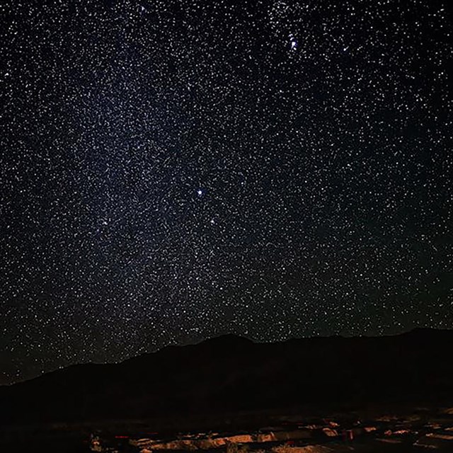 A night sky of stars over a mountain landscape.