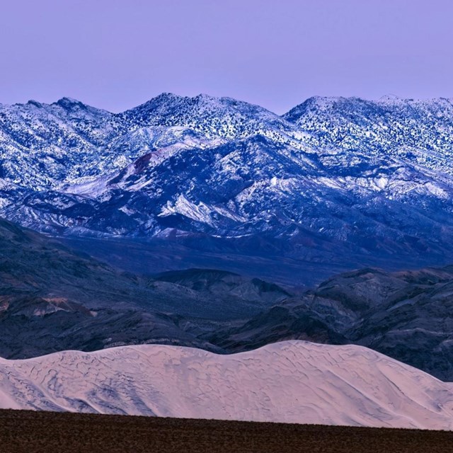 Landscape of sand dunes with snow dusted mountains in the background.NPS/J. Hallett