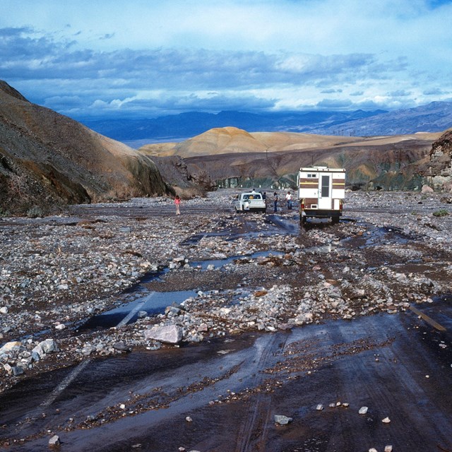Color image of flood debris cover CA-190 and two vehicles stuck on the highway. NPS/Dale Luthy