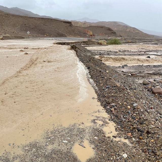Floodwaters cut across a gravelly road in a narrow desert valley. 