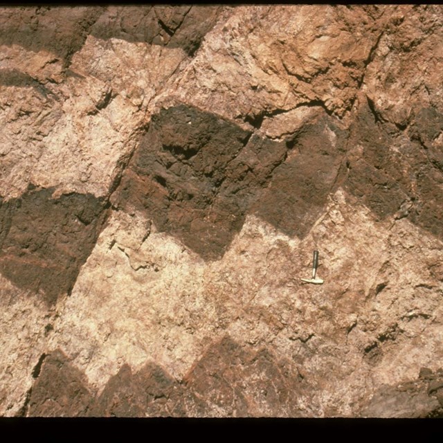 Rock layers alternate with offset light and dark brown stripes. 