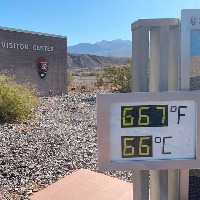 A large digital thermometer displays 667F and 66C in front of a stone building.