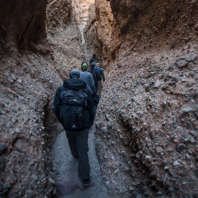 Several visitors hike through a narrow slot canyon in Death Valley National Park. NPS