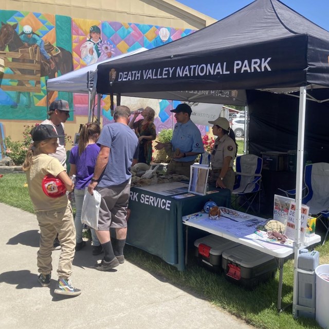 Scientist in Parks Interns staff an information table, under a pop-up tent, to engage with visitors.