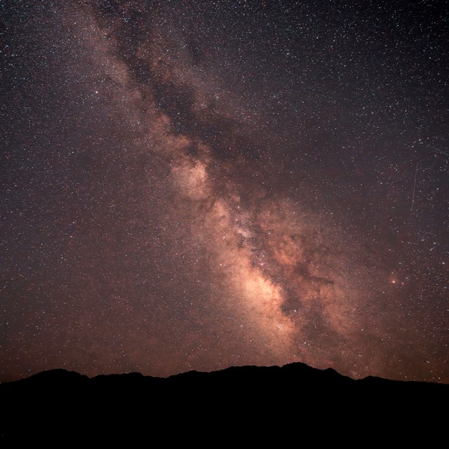 A night sky fills the frame, thick with stars. A wide, hazy band of light runs diagonally.