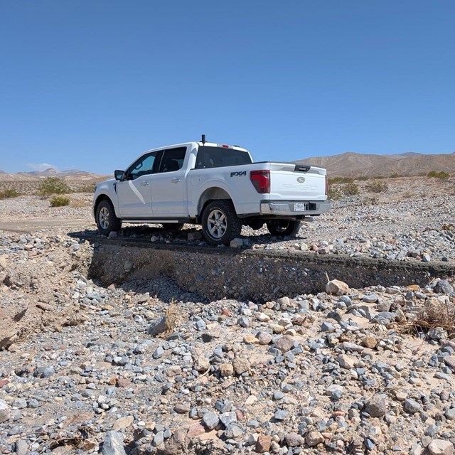 Side view of a white truck parked on a road covered in rocky debris with the downhill road shoulder 